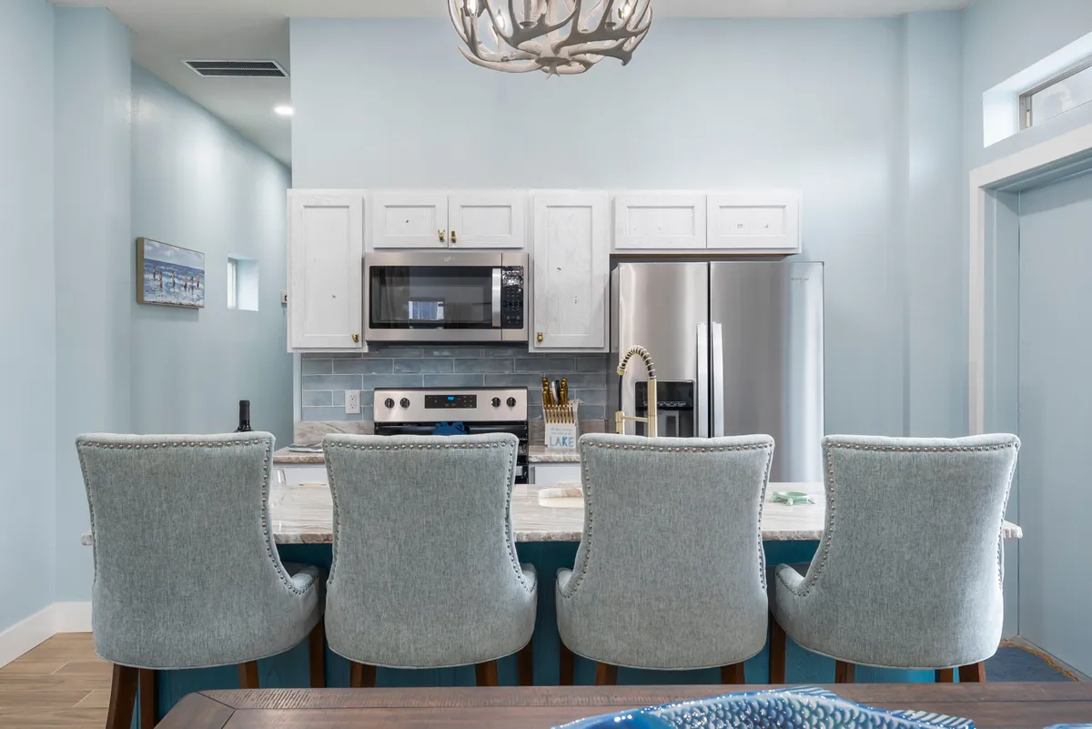 A bright, open kitchen with a spacious island, chic chandelier, and stainless steel appliances. The island offers plenty of room for meal prep or socializing, and the setting is ideal for shared breakfasts or festive dinners.