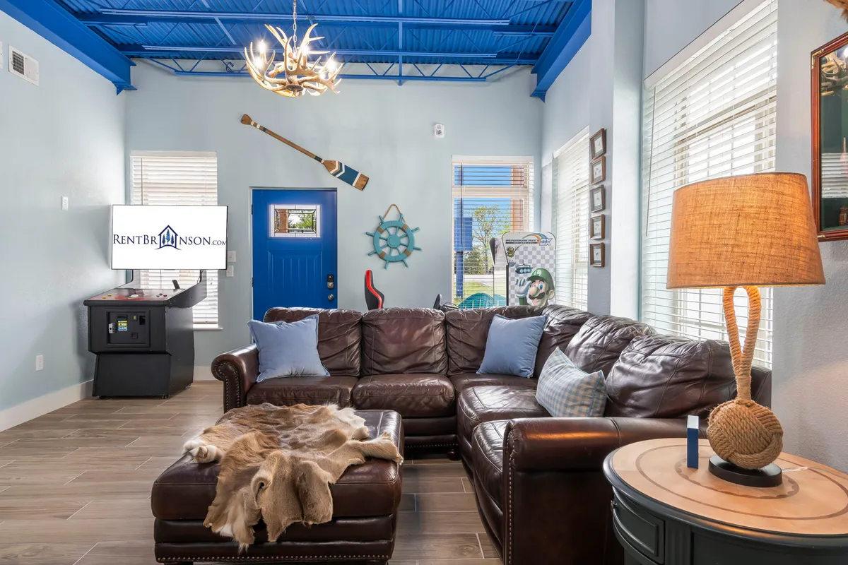 A spacious, comfortable living area with a large leather sectional sofa, blue door, modern chandelier, and decorative oars on the wall. There’s a flat-screen TV and plenty of space for group activities, socializing, or relaxing together.