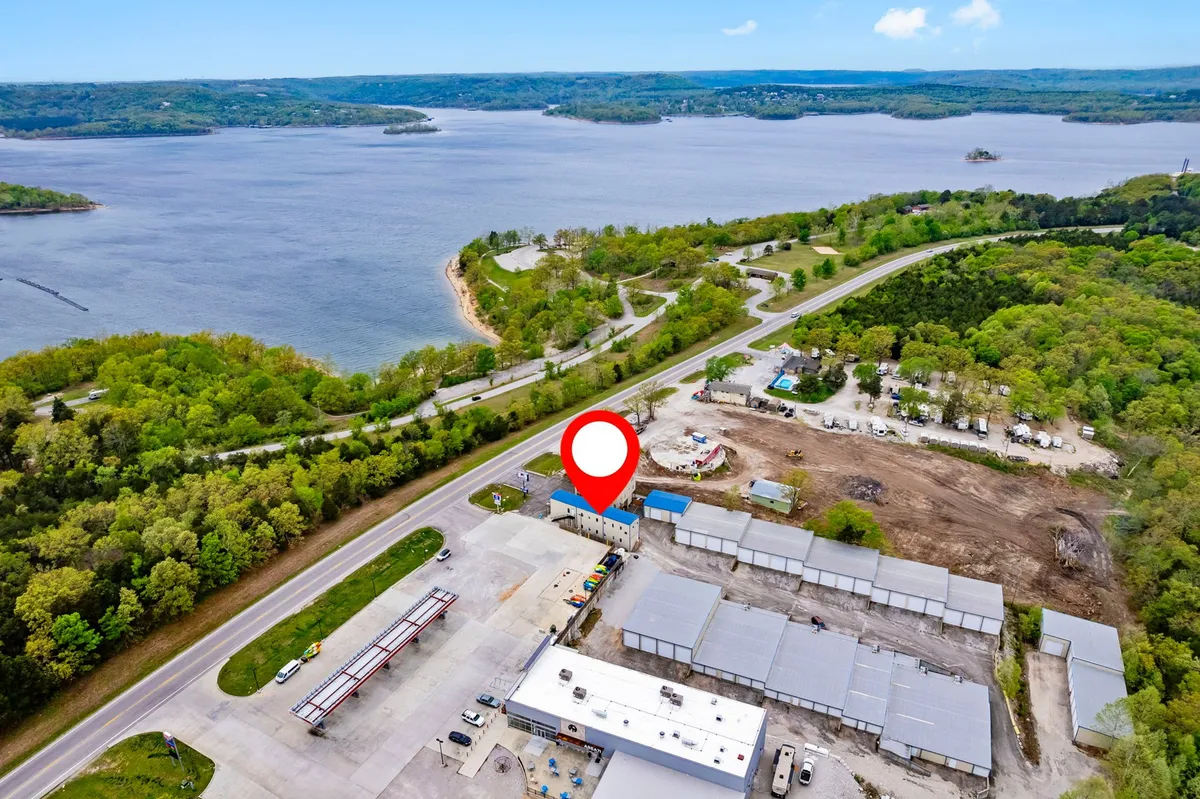 An expansive view over the lake and nearby buildings, roads, and greenery. The tranquil water, dotted with boats, is surrounded by natural beauty, and the image captures the atmosphere of a community gathered around outdoor adventure. The sky glows softly, hinting at a magical time of day.