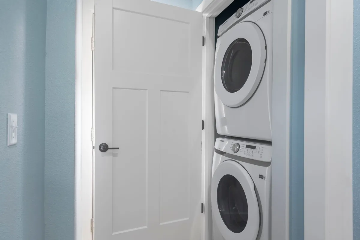 A bright and functional laundry area featuring a stacked washer and dryer, blue walls, and a white door, efficiently designed for group convenience.