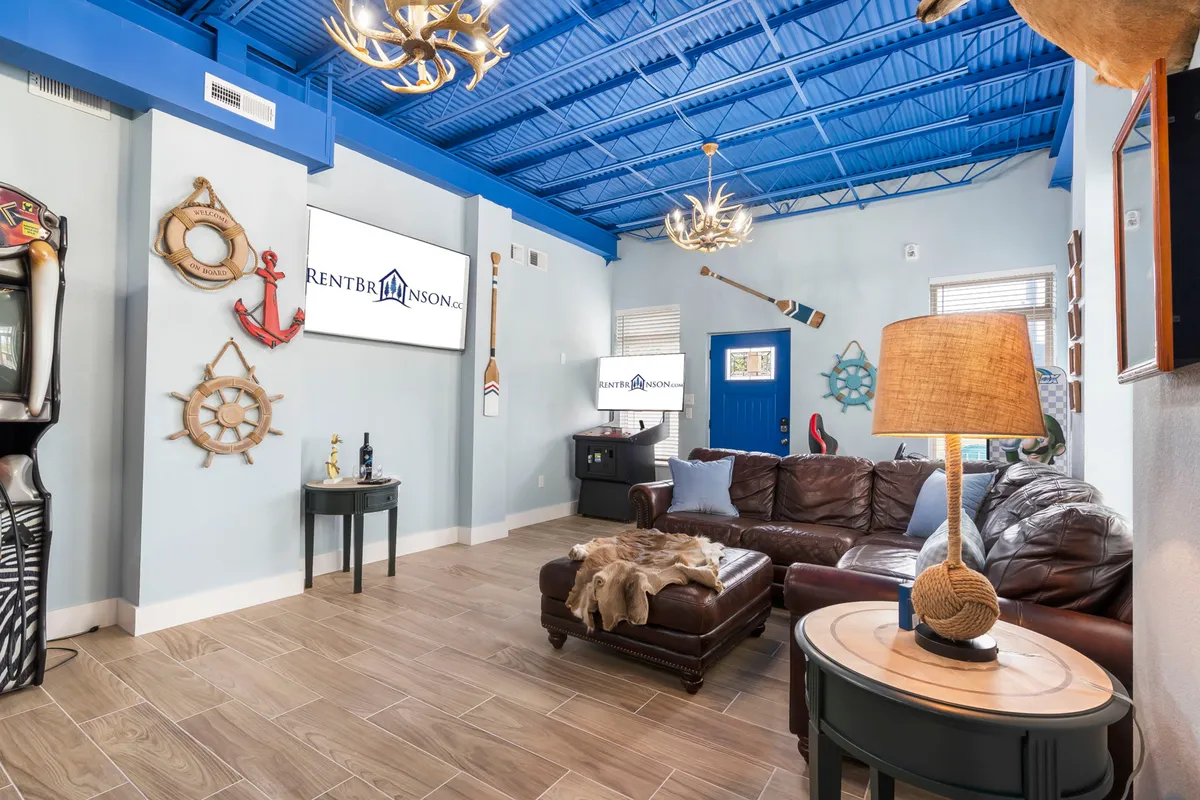 An inviting living area with a leather sofa, blue ceiling, nautical-themed decor (anchors and oars), and multiple TV displays. The arrangement encourages group activities such as watching televised events and socializing in comfort.