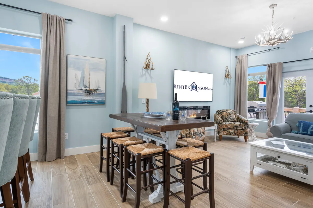 A spacious, open-plan living and dining area featuring a large dining table perfect for group meals, a comfortable seating area with plush sofas, a television for entertainment, and tasteful artwork on the walls. The space is filled with natural light, creating an inviting and cozy atmosphere ideal for socializing and relaxing after outdoor adventures.