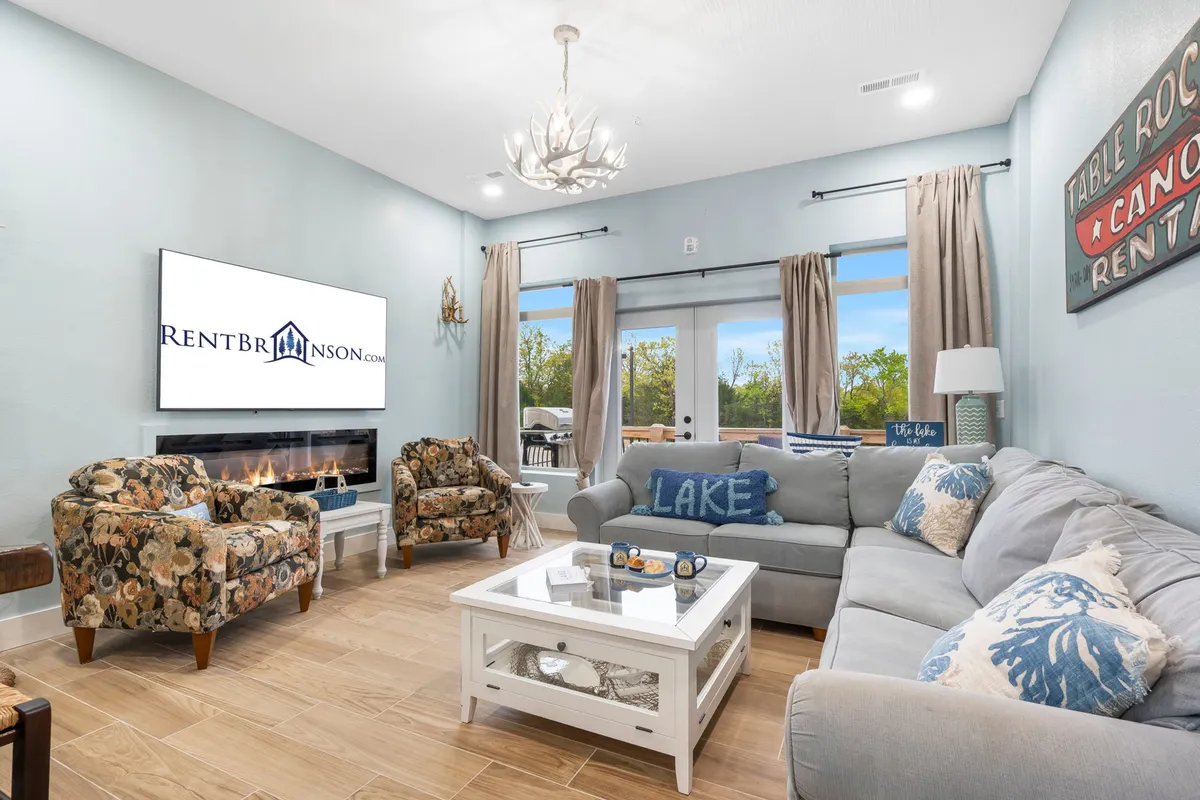 A comfortable living area with a sofa adorned in lake-themed pillows, a glowing fireplace, decorative chairs, and a television. The ambiance is cozy—ideal for relaxing evenings, game nights, or movie marathons by the fire.